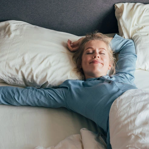 Lächelnde junge Frau, die an einem sonnigen Morgen ihre Arme im Bett streckt